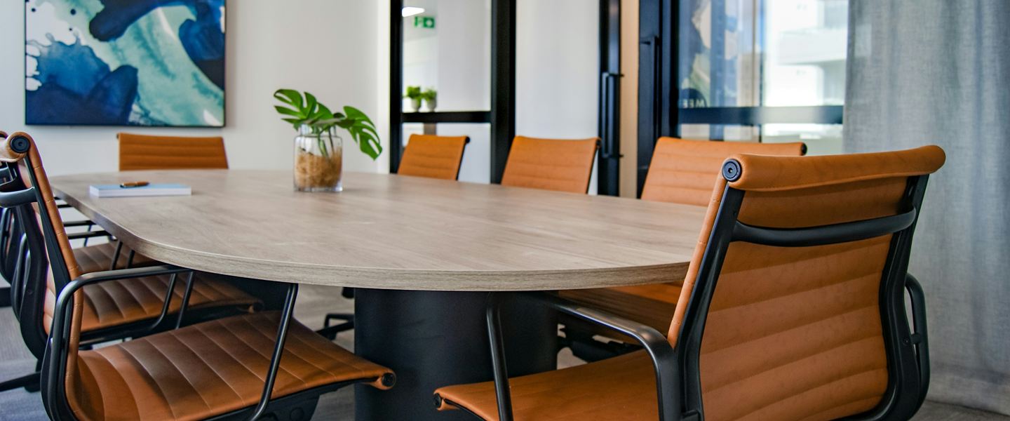 Meeting room with a pale wooden table, tan leather chairs and glass partitions