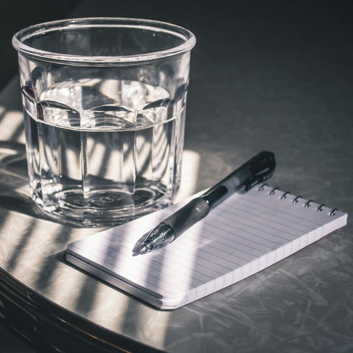 Glass of water, pen and notepad on a table in slatted sunlight