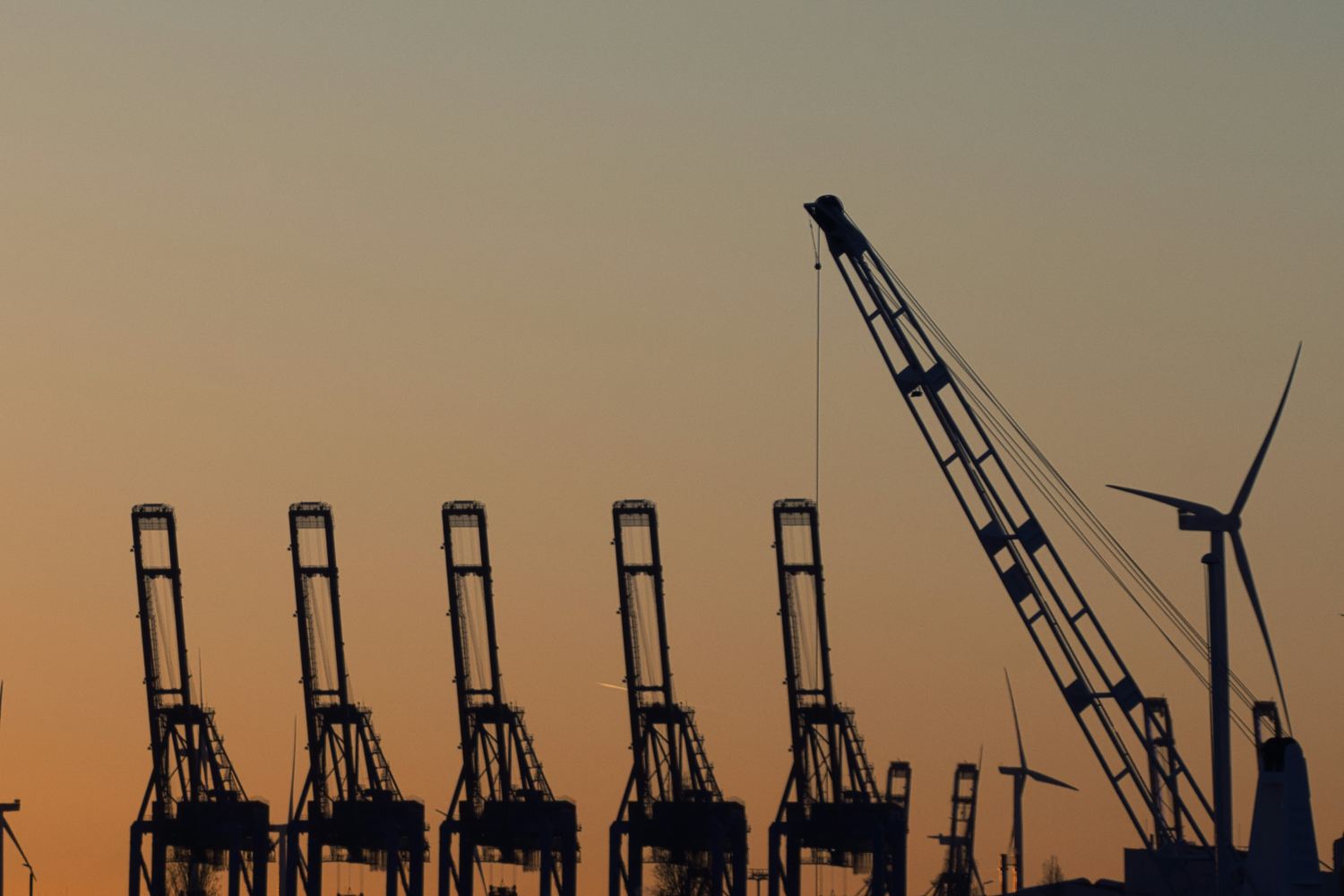 Container cranes at a seaport silhouetted against an orange dusk sky