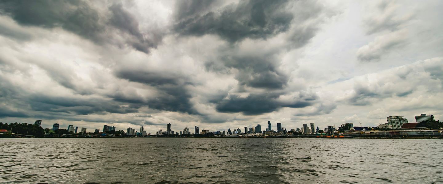 Dark storm clouds gathering over Bangkok's towers, seen across the river