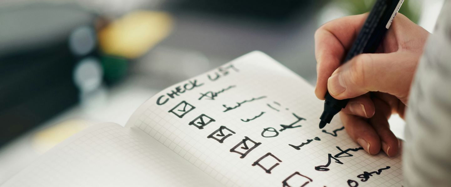 Hand ticking boxes on a handwritten checklist in a notebook