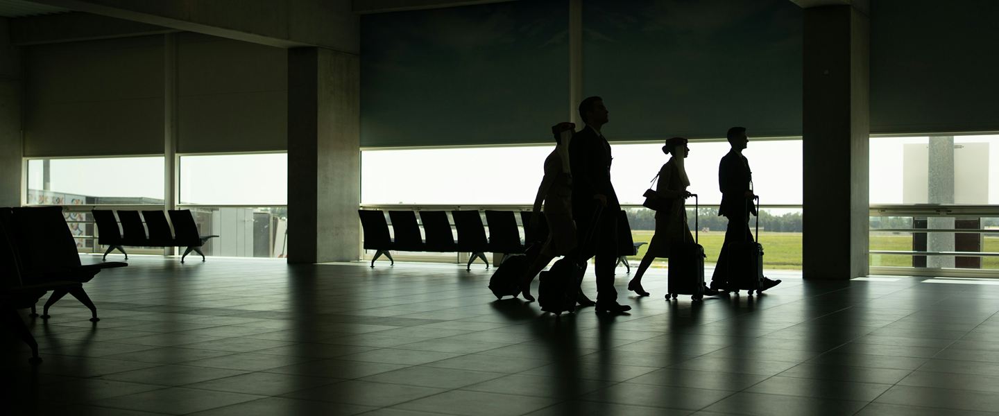 Silhouettes of travellers with suitcases crossing a quiet airport terminal