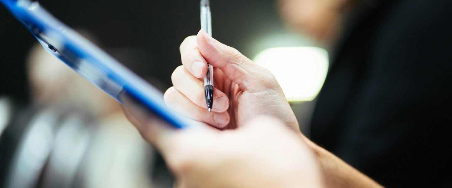 Hand holding a ballpoint pen over a blue clipboard
