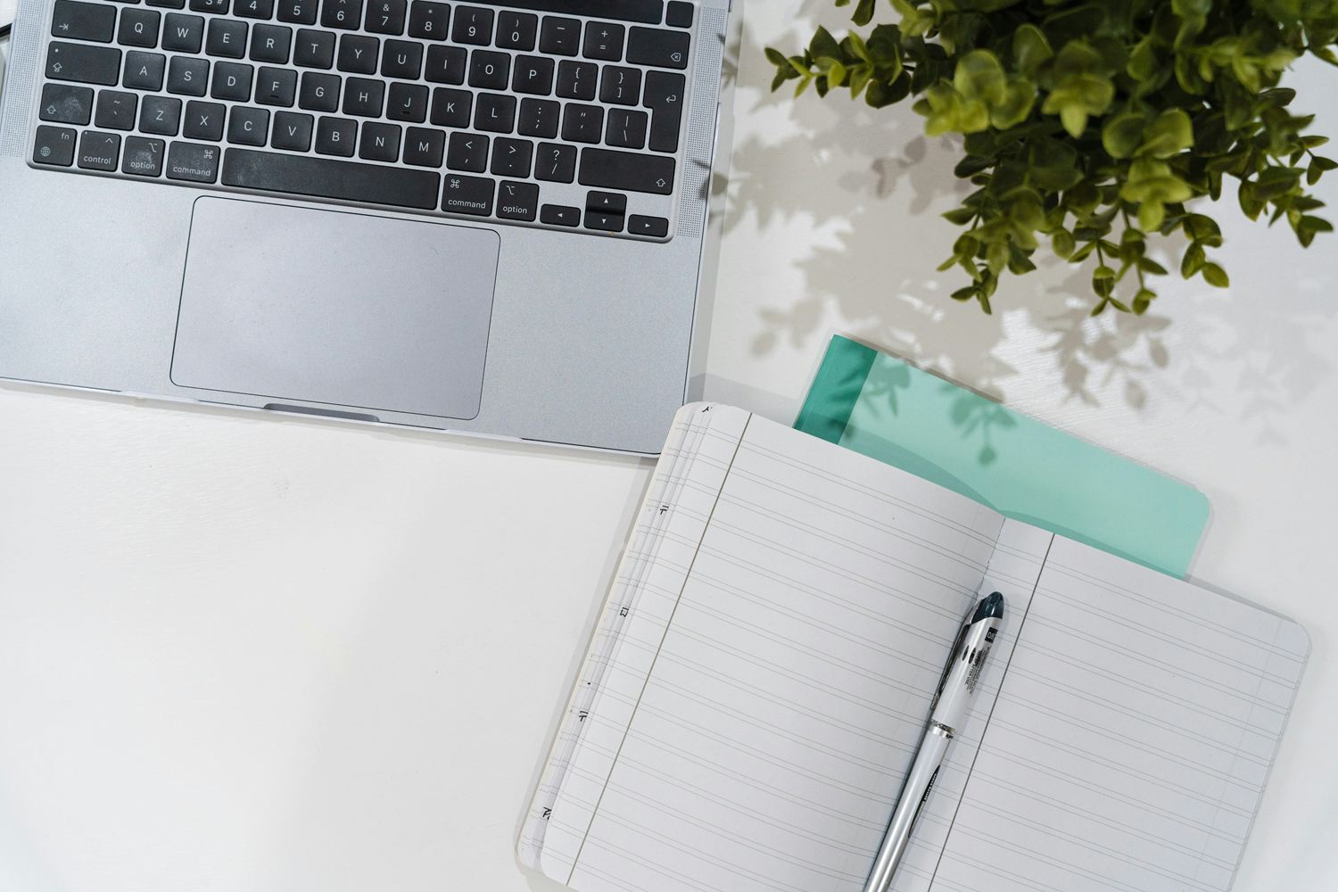 Laptop, open ruled notebook and pen on a white desk