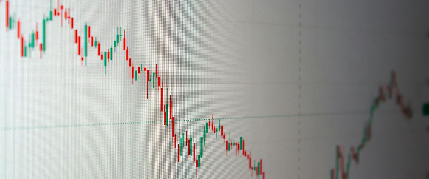 Red and green candlestick price chart on a pale screen, seen at an angle
