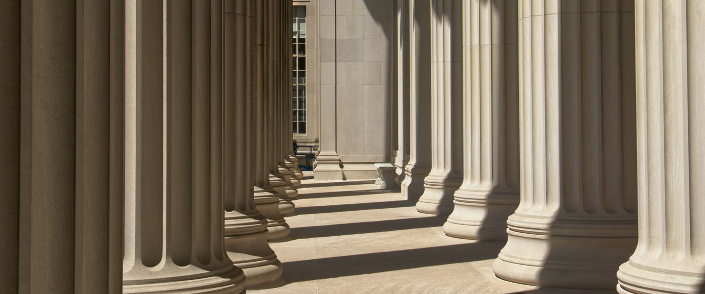 Row of fluted stone columns in sunlight casting shadows across a colonnade