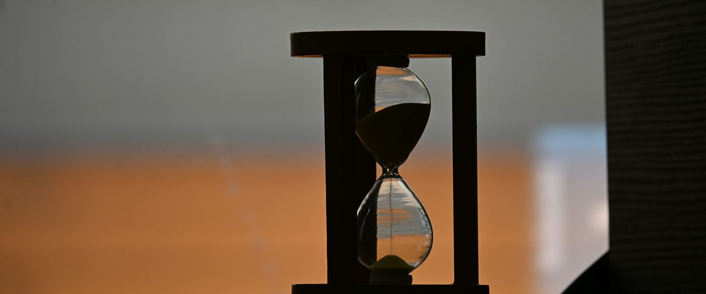 Hourglass in a wooden frame silhouetted against soft evening light