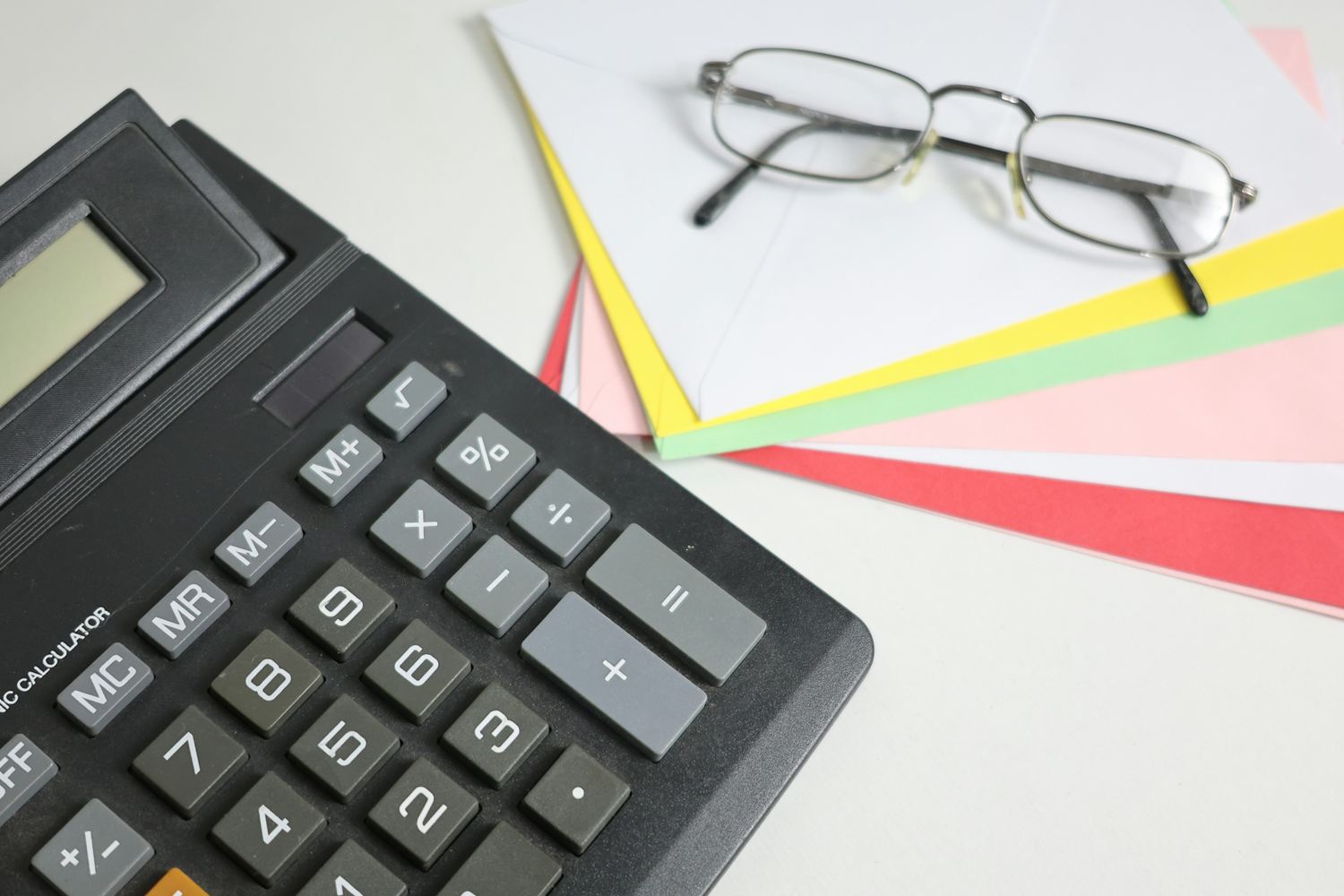 Desk calculator with a percent key beside reading glasses on coloured paper