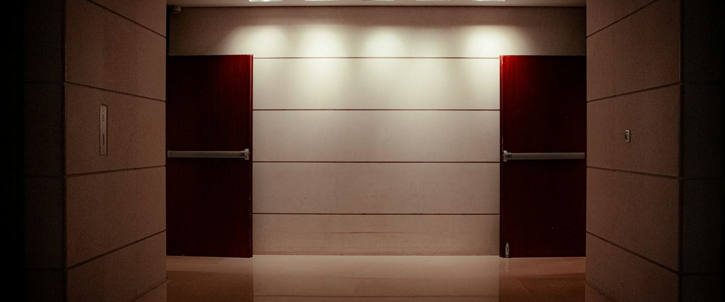 Two identical dark red doors on either side of a lit wall