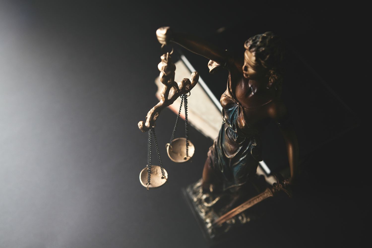 Bronze statuette holding a pair of balance scales against a dark background