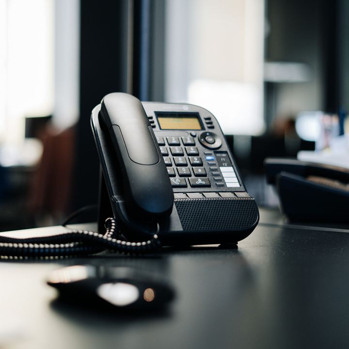 Desk telephone on a dark desk with office screens blurred behind