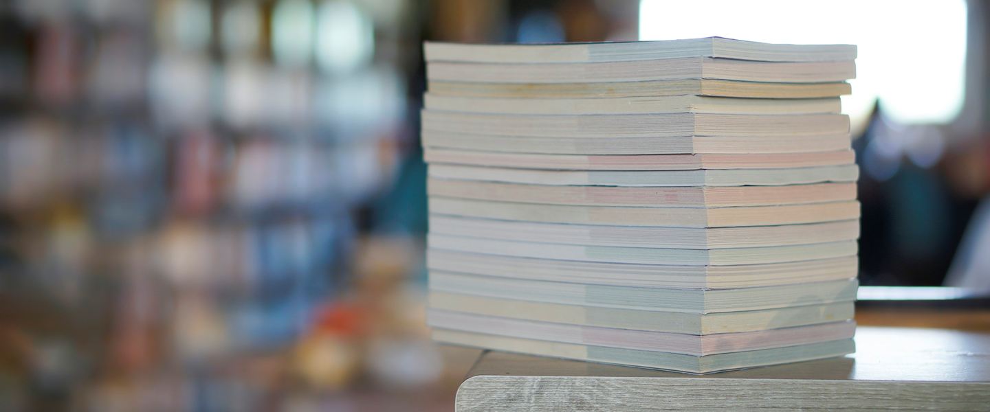 Stack of bound reports on a desk with bookshelves blurred behind
