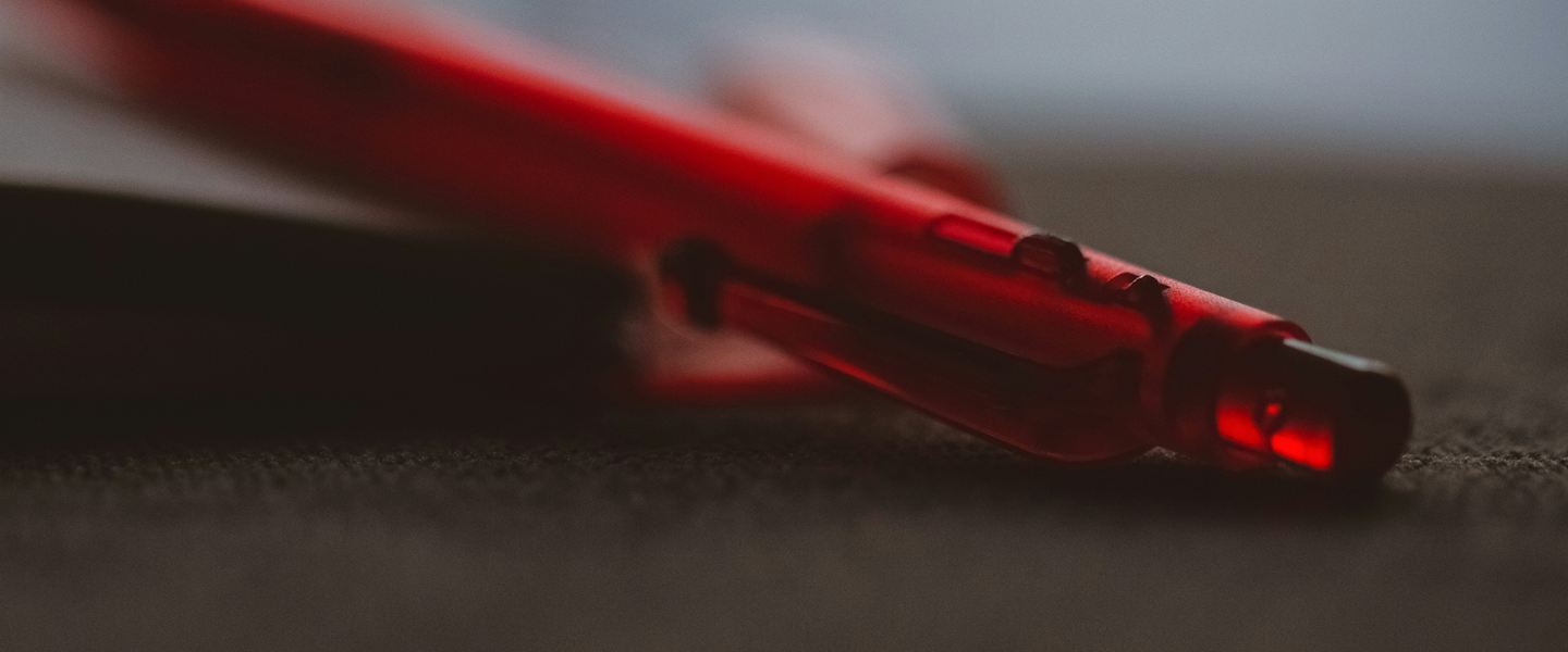 Close-up of a red pen resting against a dark notebook