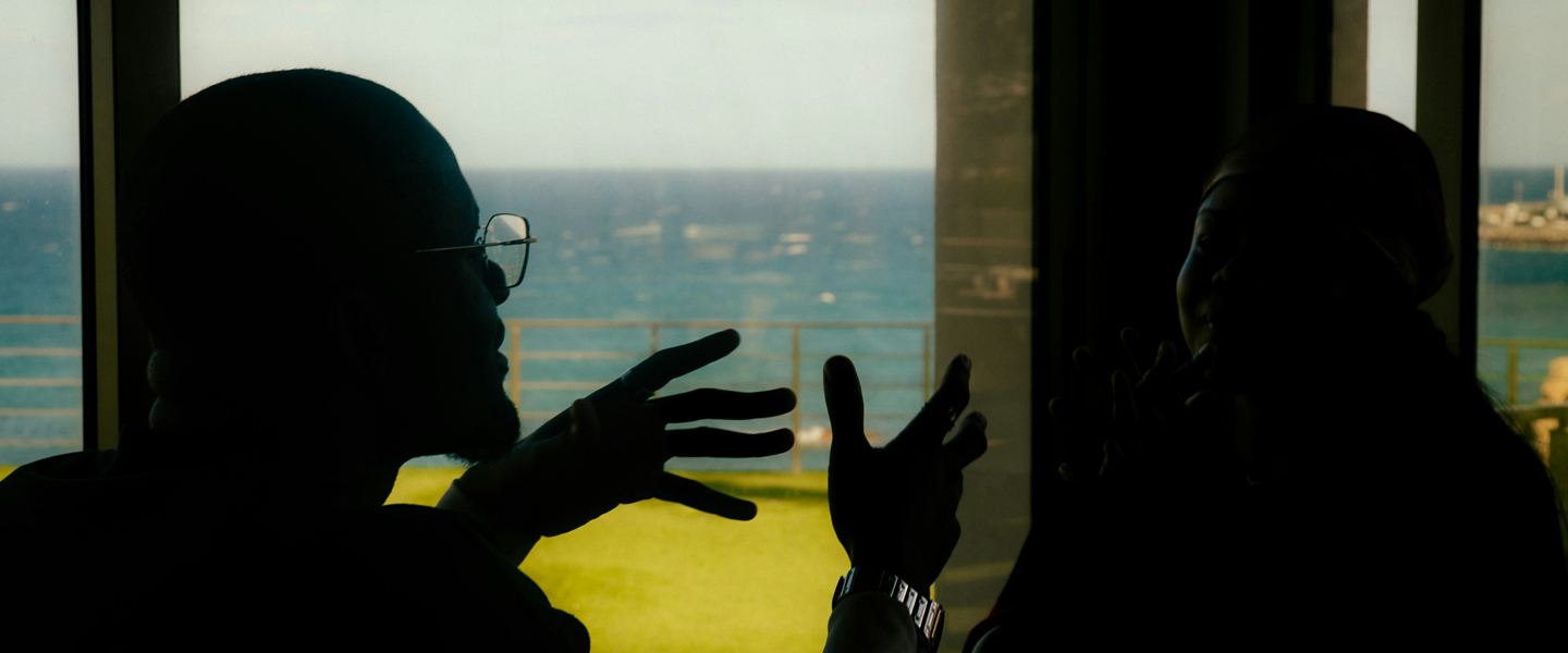 Two people in silhouette talking beside a window overlooking the sea