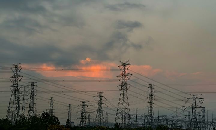 High-voltage transmission towers under a cloudy sky tinged pink at sunset