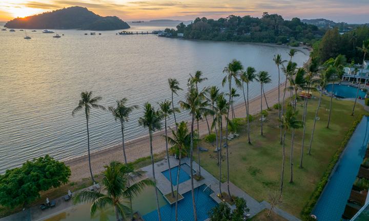Beachfront resort with pools and coconut palms at sunset, seen from above