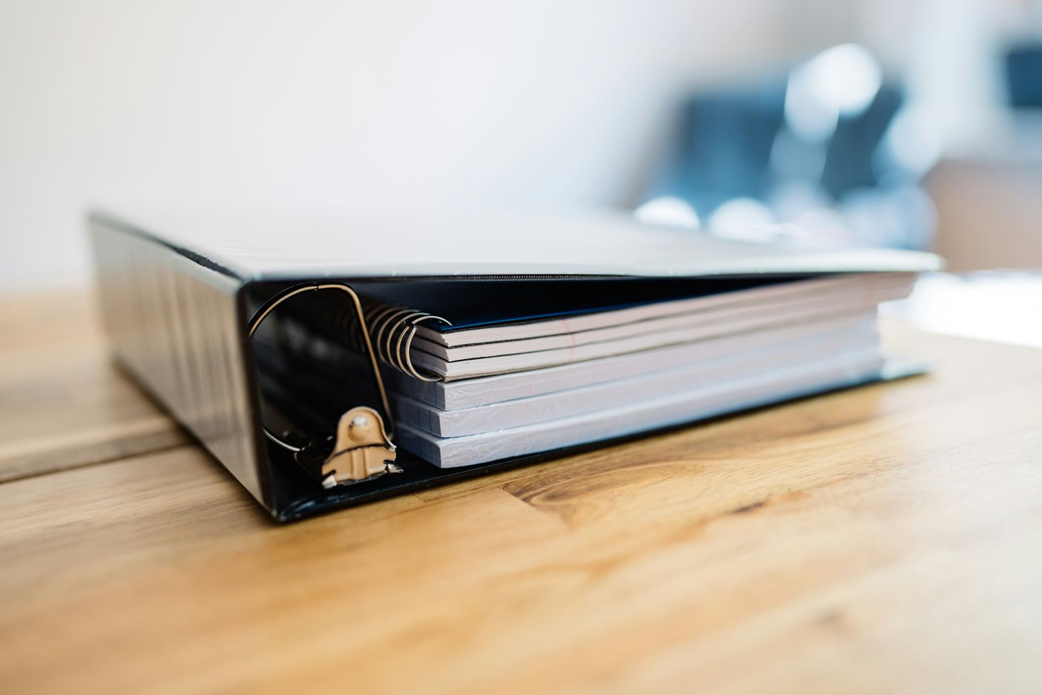 Black ring binder holding stacks of paper on a wooden desk
