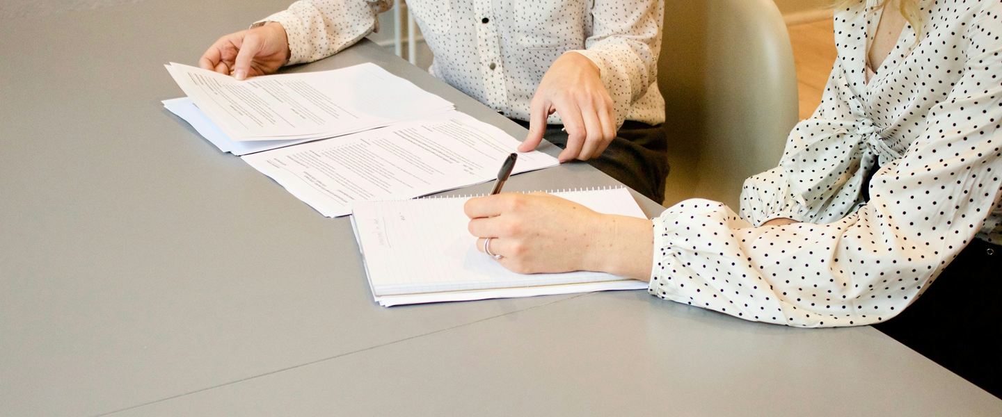 Two people reviewing printed documents at a table, one writing notes
