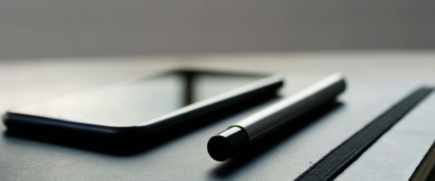 Phone and pen resting on a notebook on a desk by a window
