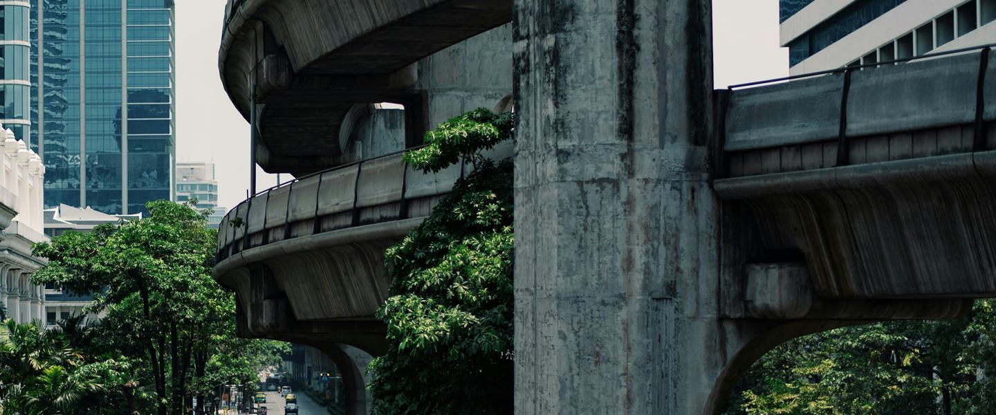 Concrete elevated viaduct curving past a glass office tower in central Bangkok